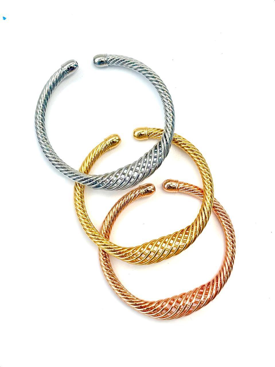 Three twisted cuff bracelets in silver, gold, and bronze colors, displayed against a white background.