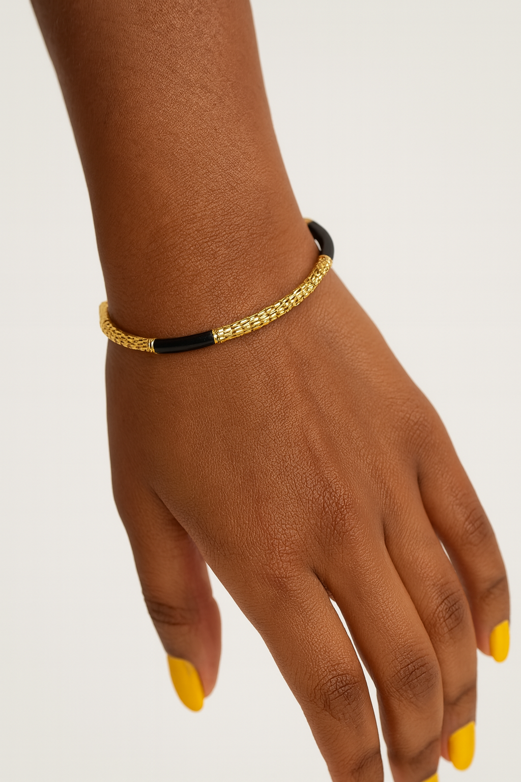 Lydia Cuff gold and black bracelet on a wrist with a neutral background. Side view of Lydia Cuff showcasing high shine gold plating and enamel drops oil coating.