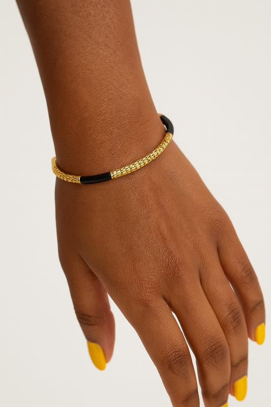 Lydia Cuff gold and black bracelet on a wrist with a neutral background. Side view of Lydia Cuff showcasing high shine gold plating and enamel drops oil coating.