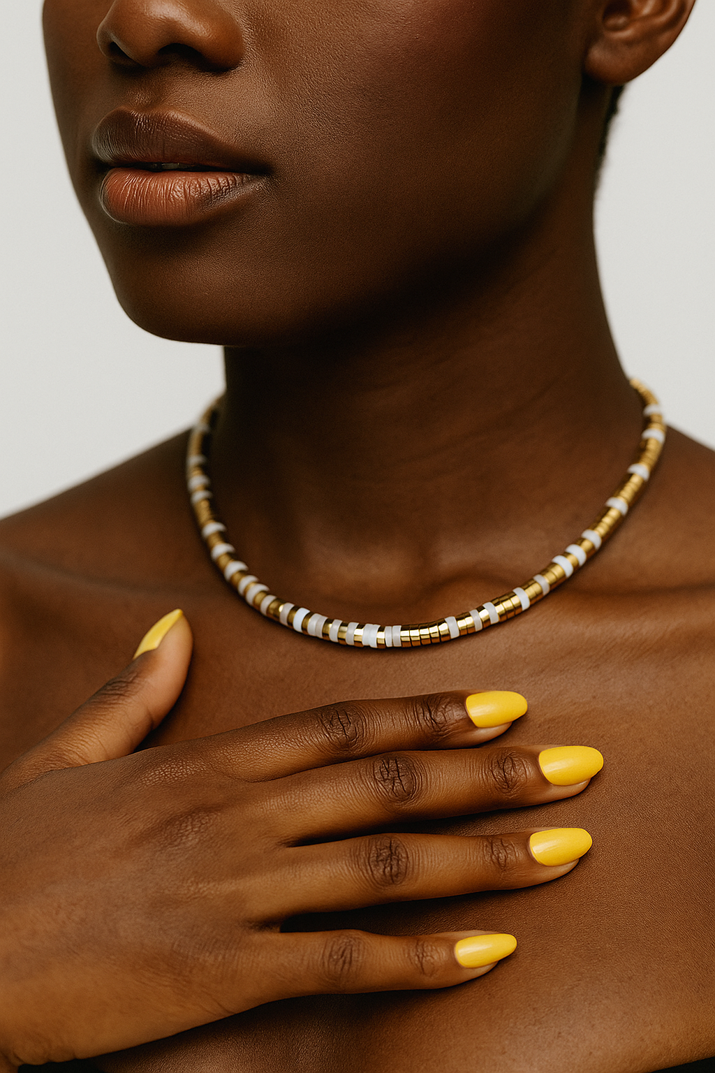 Close-up of a women wearing a beaded necklace with a neutral background. White and gold minimalist beaded bracelet from the Eona Set