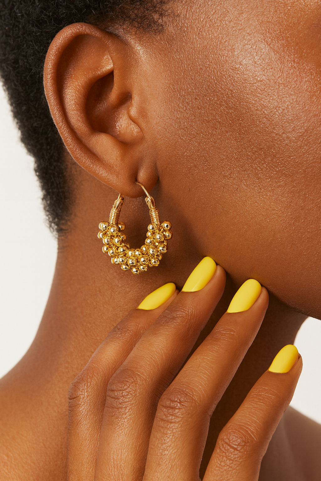 Close-up of a person wearing gold hoop women earrings with a neutral background. Lightweight gold bead hoop earrings for everyday wear