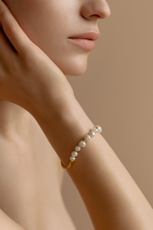 Close-up of irregular natural pearls with gold beads on the Harper Bracelet. Pearl bracelet on a person's wrist with a neutral background