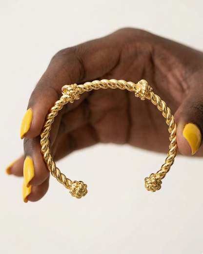 female Gold braided bracelet on a hand with yellow nail polish against a white background