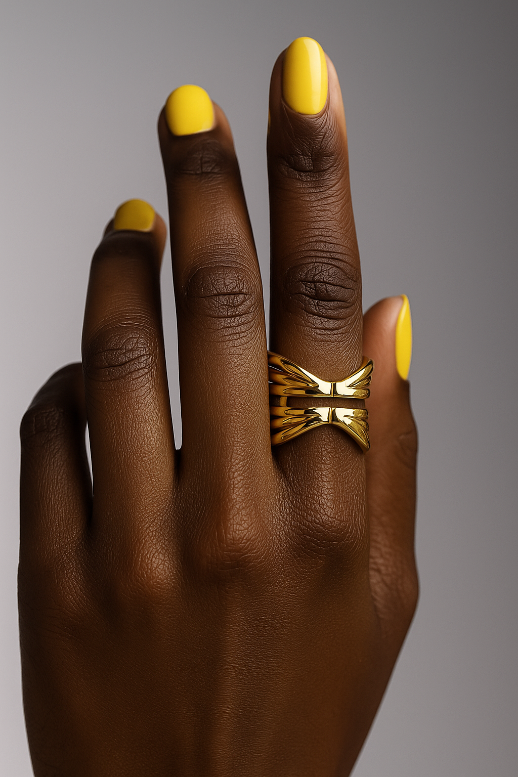 Hand with gold ring and yellow nail polish on a gray background. Bold contemporary gold statement ring Kira Ring by Miriama.
