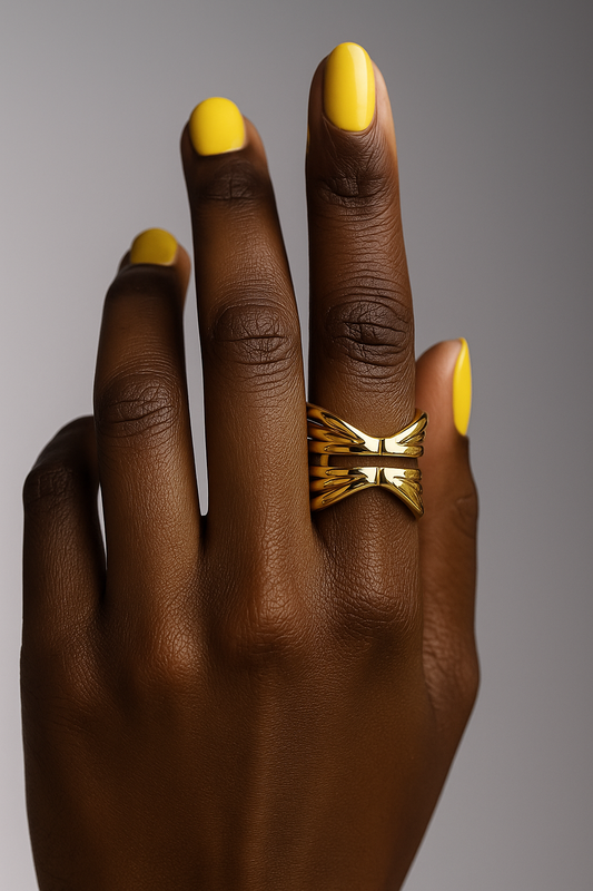 Hand with gold ring and yellow nail polish on a gray background. Bold contemporary gold statement ring Kira Ring by Miriama.