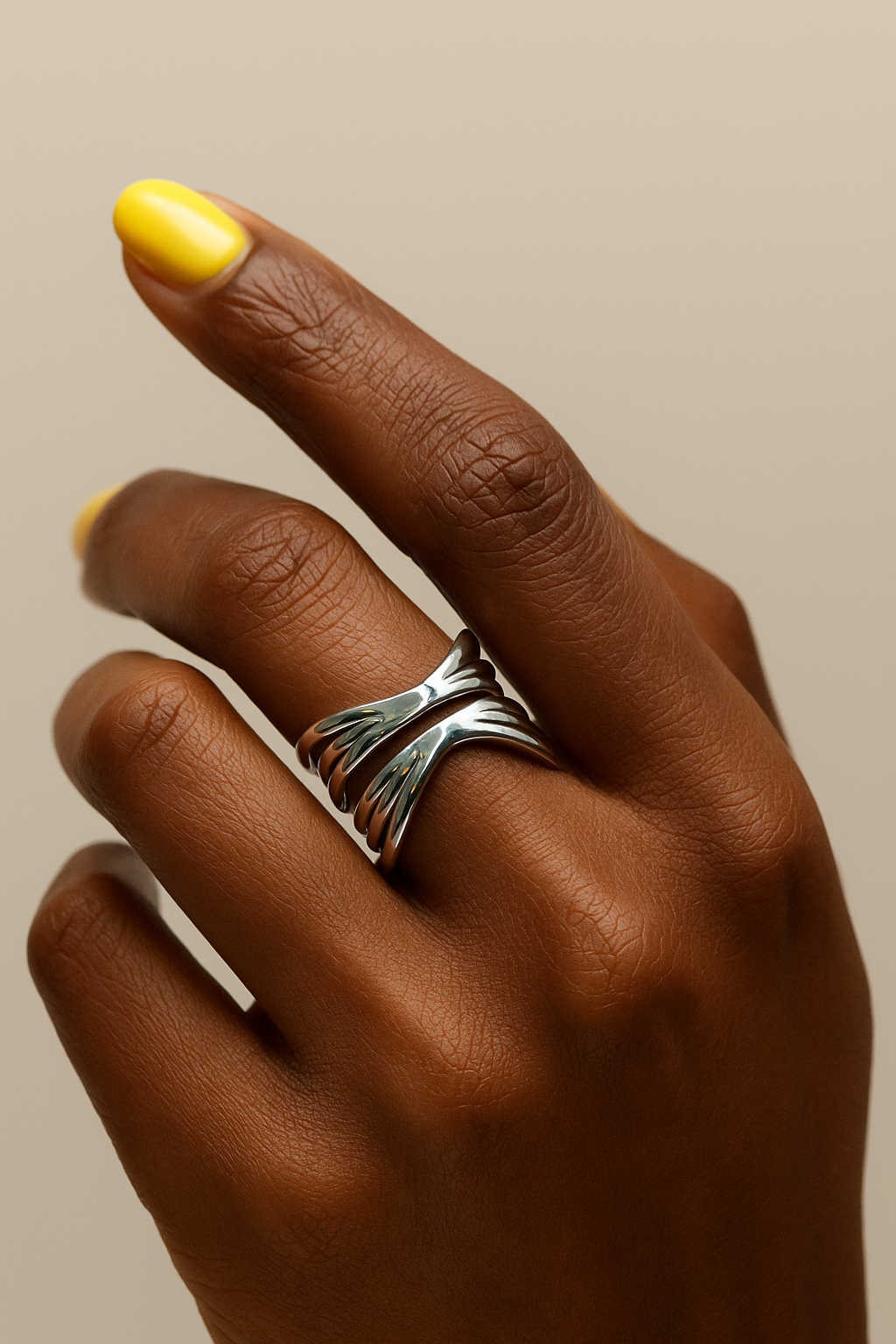 Hand wearing a silver ring with a yellow nail polish on a beige background. Silver layered band Kira Ring modern statement jewelry for women.