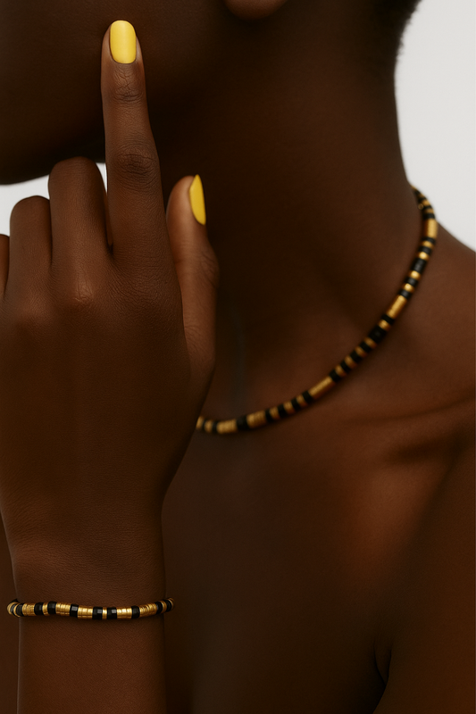 Person women a black and gold beaded necklace and bracelet with yellow nail polish. Close-up of Eona Black Set showing gold and black stainless-steel beads