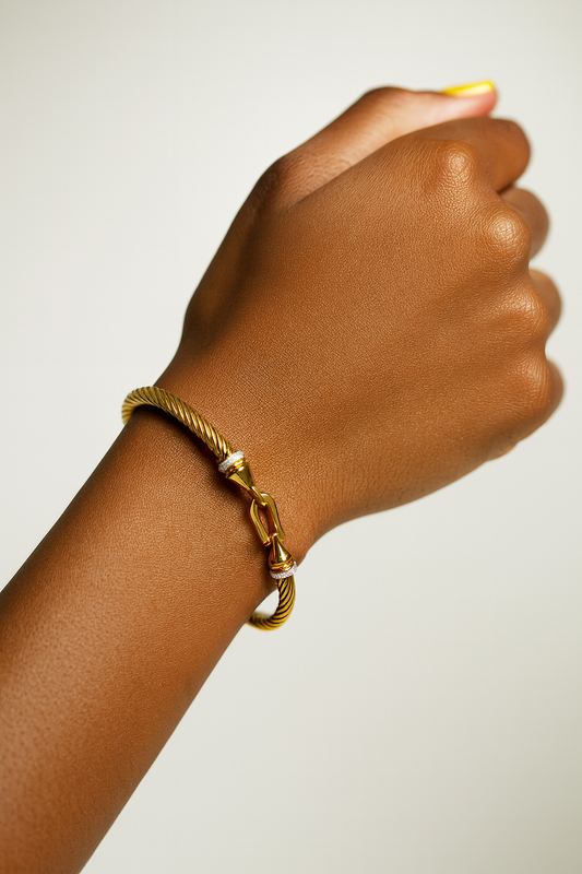 Gold bracelet on a wrist against a plain background. Minimalist gold Scarlett Bracelet with smooth curved finish. Scarlett Bracelet in a model hand.