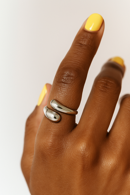 Hand wearing a silver ring with yellow nail polish on a white background.Silver Sia Ring – sculptural modern open-ended ring with high-polish finish.