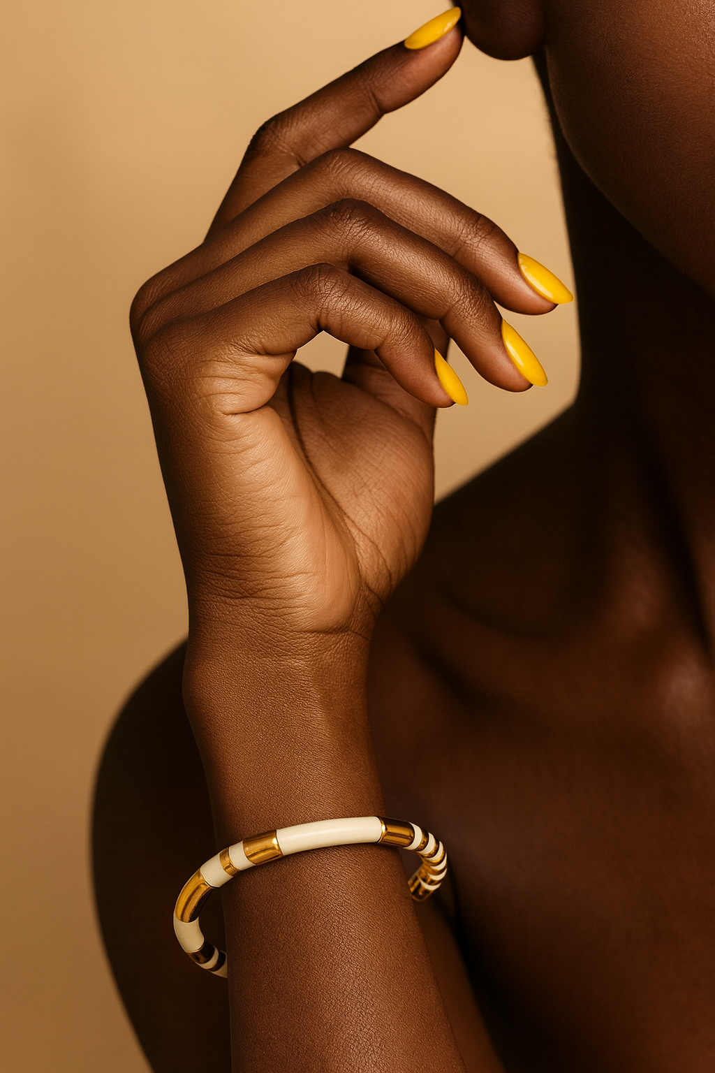 Close-up of white enamel and gold segmented cuff bracelet. Hand with yellow nail polish wearing a gold and white bracelet on a beige background